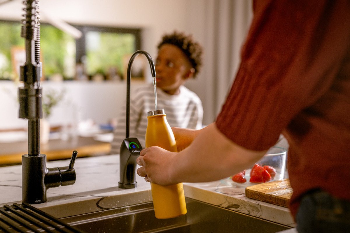 Person filling water bottle at kitchen drinking water system